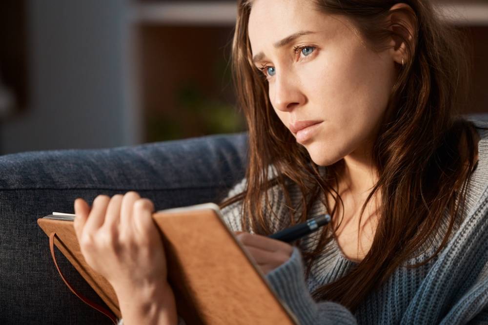 Home, woman and thinking with journal for mental health, stress management and depression in living room.