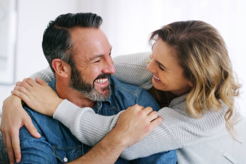 Relax, funny and hug with couple on sofa in home for bonding, connection and support.