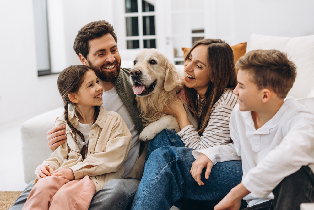 Family enjoying quality time together, embracing and laughing with their beloved pet golden retriever in the comfort of their home,